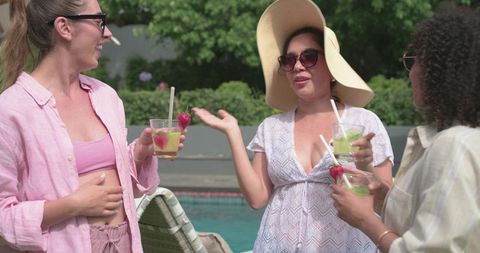 Poolside friends sipping green cocktails, wearing sunhat and shades, enjoying summer chat