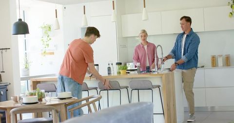Friends adjusting bar stools and washing dishes at bright modern open-plan kitchen island