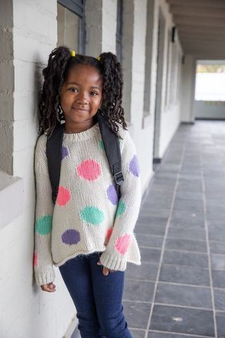 Young Girl in Colorful Sweatshirt with Backpack in School Corridor