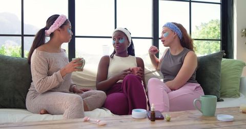 Friends enjoying cozy at-home spa moment with under-eye patches, loungewear and mugs