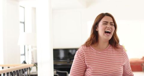 Sunlit laughing woman in pink striped top in modern living room with piano