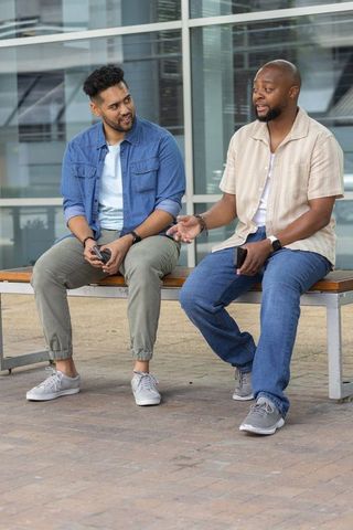 African american friends chatting on urban bench using smartphones and smartwatches