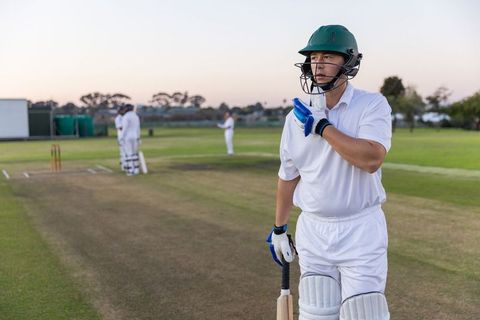 Batsman preparing at dusk on worn cricket pitch holding bat in white kit