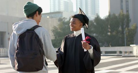 African american graduate shaking hands with friend on urban campus celebrating diploma