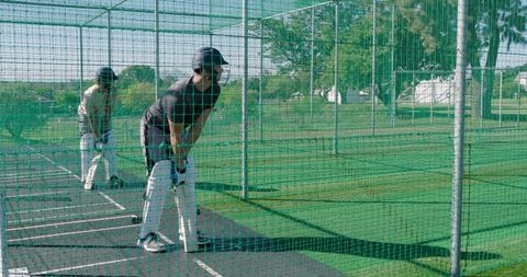 Two male cricketers practicing batting inside outdoor net cage during team training session