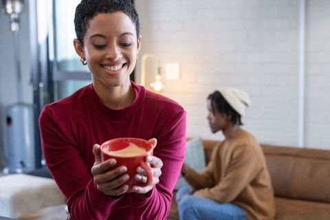 African american woman enjoying latte while partner scrolling smartphone in living room