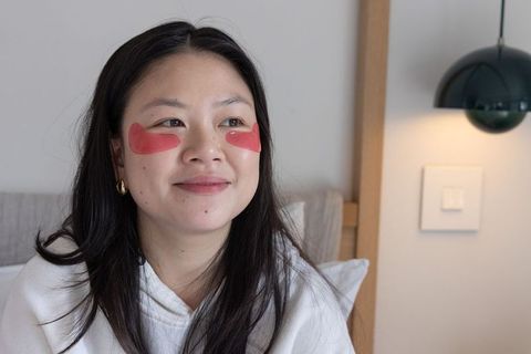 Asian woman wearing red hydrogel under-eye patches enjoying cozy home skincare routine