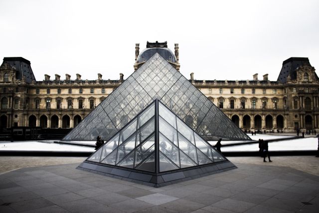 Louvre Museum Pyramid entrance features iconic glass pyramid contrasting with historic building backdrop in Paris, France. Great for travel, architecture, and cultural images showcasing famous landmarks and sights.