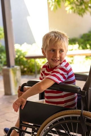 Smiling blond child in wheelchair enjoying sunny courtyard moment of independence