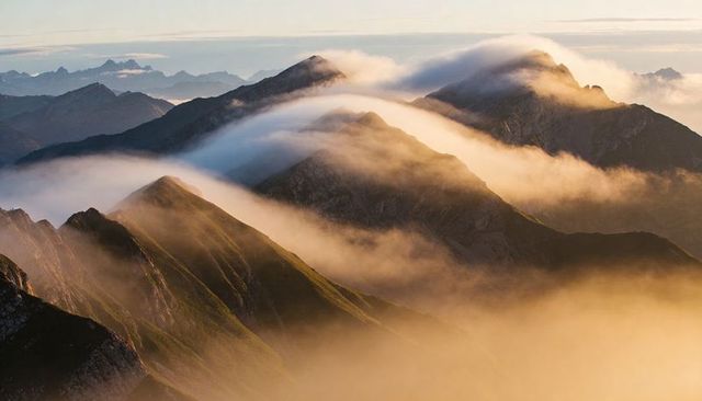 Golden mist rolling over alpine ridges at sunrise, layered mountain panorama