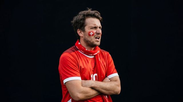 Tense swiss football fan wearing number 10 jersey and scarf showing swiss cross face paint