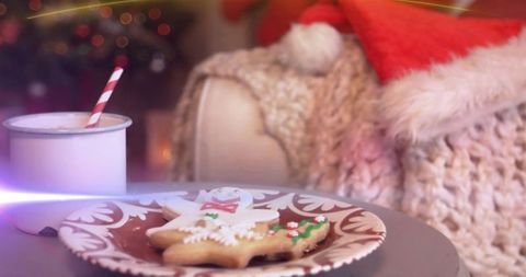 Displaying cozy christmas cookies and mug beside knit blanket and santa hat with bokeh lights