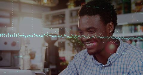 Smiling man using laptop and smartphone in coffeehouse with data analytics overlay, warm bokeh