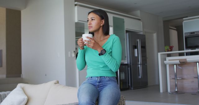 Young Woman Leaning on Sofa with Coffee Cup in Open-Plan Kitchen - Download Free Stock Images Pikwizard.com