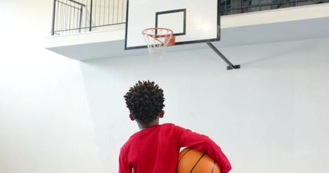 Young Basketball Player Holding Ball Underneath Gym Hoop