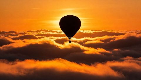 Hot air balloon floating above golden cloudtops at sunset with dramatic backlit silhouette