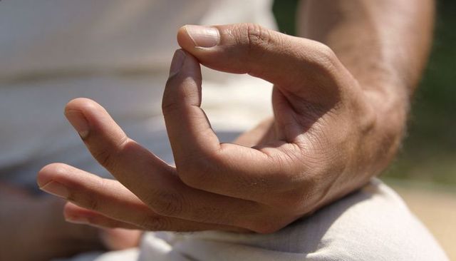 Right hand forming meditation mudra on knee practicing mindfulness outdoors in park