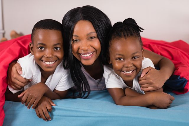 Mother and children lying on bed, smiling and enjoying time together. Perfect for family-oriented content, parenting blogs, advertisements for home products, or articles about family bonding and happiness.