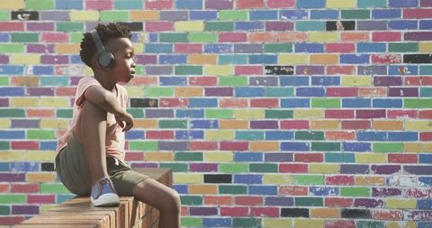 Young Boy Relaxing Listening to Music Beside Colorful Brick Wall