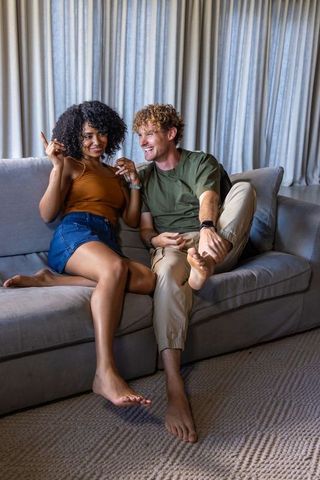 Young couple laughing on sofa sharing smartwatch moment and relaxed conversation at home