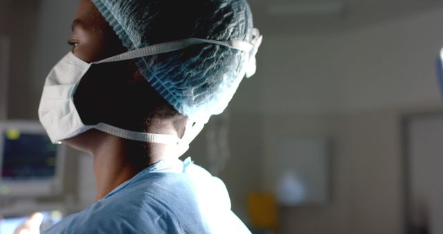 An African American surgeon dressed in surgical mask, scrubs, and protective cap focused during surgical procedure in an operating room. Ideal for use in articles, blogs, and marketing materials related to healthcare, medical professionals, and surgical procedures.