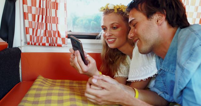 A young Caucasian couple is engaged with a smartphone, sharing a moment of connectivity in a cozy setting, with copy space. Their smiles suggest they are enjoying a personal conversation or entertaining content on the device.