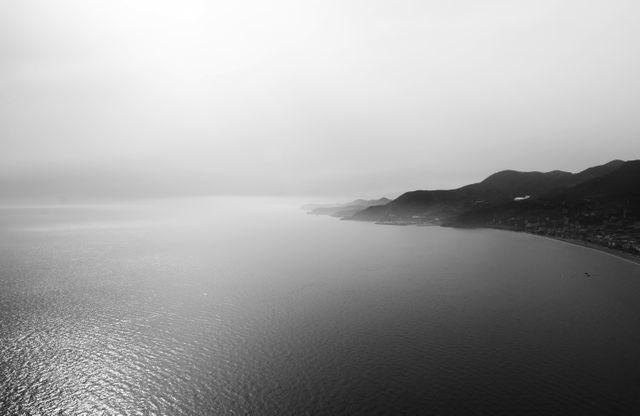 Monochrome aerial view showcases a tranquil coastal landscape with mountains meeting the sea. Ideal for travel brochures, nature-themed advertisements, or home decor prints, evoking a sense of calm and vastness.
