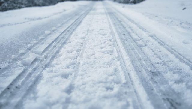 Low-angle snow-covered road showing converging tire tracks, slush and winter texture perspective