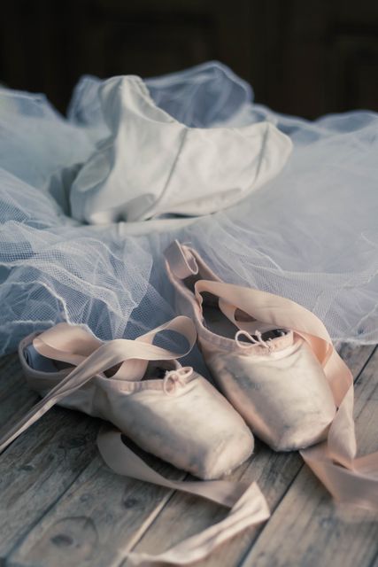 Pointe shoes and a ballet tutu arranged on a wooden floor, creating a classic and elegant ballet scene. Useful for themes related to dance, classical ballet, performing arts, and feminine grace. Ideal for marketing materials, artistic publications, or social media posts celebrating ballet and dancing.
