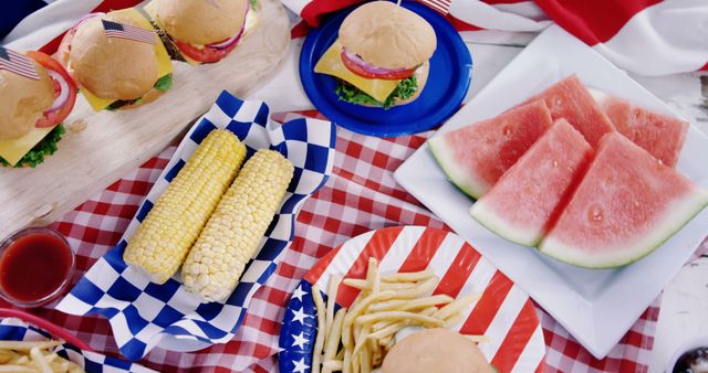 Scene of patriotic picnic table featuring burgers topped with American flags, watermelon slices, corn on the cob, and fries. Ideal for illustrating summer parties, Independence Day celebrations, or backyard barbecues.