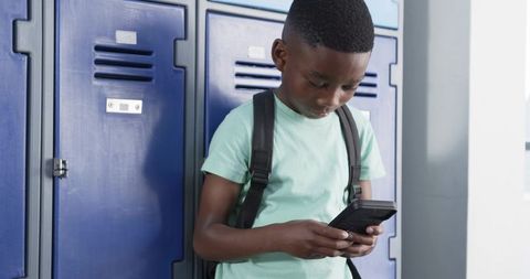 Middle school student standing by blue lockers using smartphone while wearing backpack