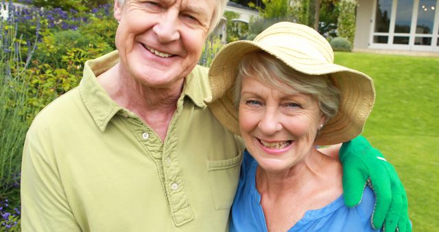 Smiling senior couple standing together in a lush garden under bright summer sunlight. Ideal for illustrating themes of retirement, outdoor hobbies, healthy living, or companionship among elderly couples. Perfect for use in brochures, advertisements, or articles related to gardening, senior lifestyles, or family values.