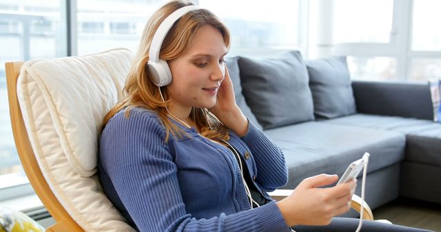 Woman sitting in living room listening music on mobile phone