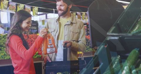 Couple selecting fresh carrots at farmers market holding black basket and smiling