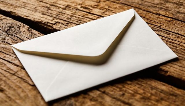 Single white envelope resting diagonally on rustic wooden planks, warm grain and shadow