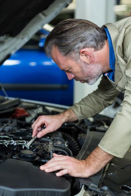 Mechanic working on a car engine in a repair garage, showcasing expertise and attention to detail. Ideal for use in automotive service advertisements, repair shop promotions, and articles about car maintenance and professional mechanics.