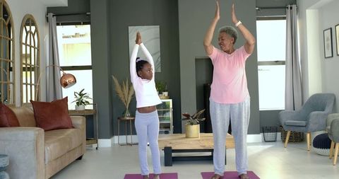Grandmother and granddaughter practicing yoga together in living room home workout wellness