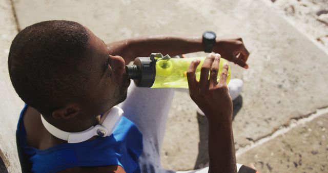 African american man sitting and drinking from water bottle taking break in exercise outdoors - Download Free Stock Photos Pikwizard.com