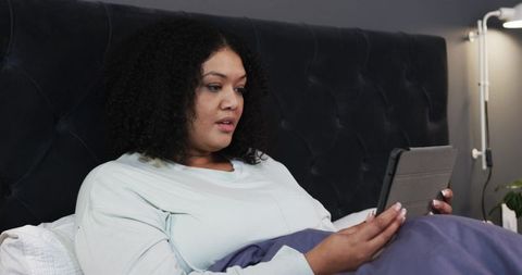 Woman Relaxing in Bed Reading Tablet in Cozy Minimalist Bedroom with Tufted Headboard
