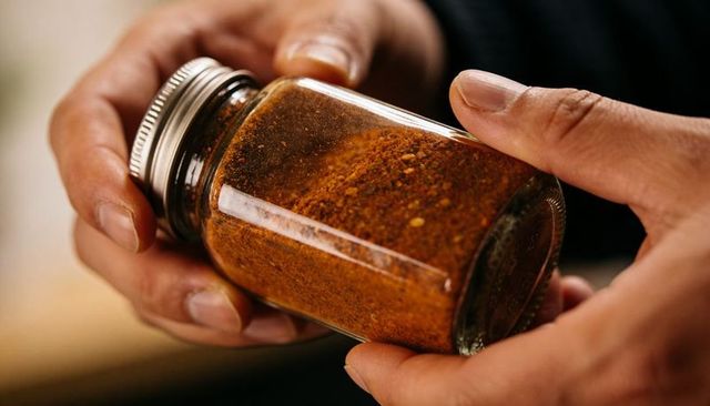 Holding glass spice jar containing smoky paprika seasoning, closeup hands inspecting