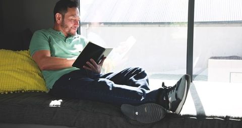 Man relaxing on sofa with tablet by sunlit window