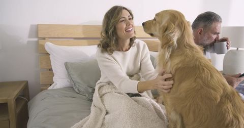 Senior Couple Relaxing with Happy Golden Retriever on Cozy Bed