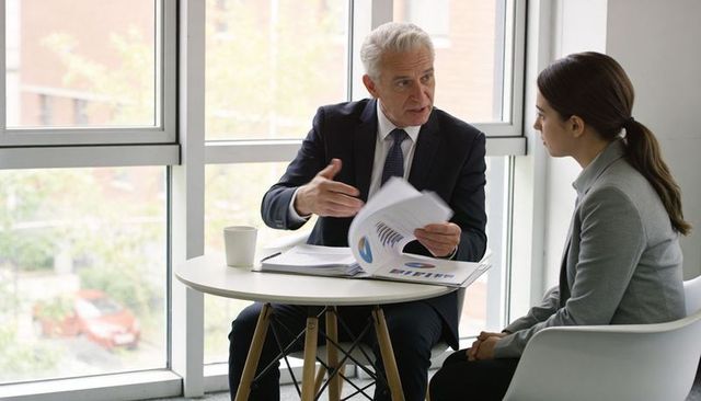 Senior executive presenting charts and reports to junior colleague in modern office