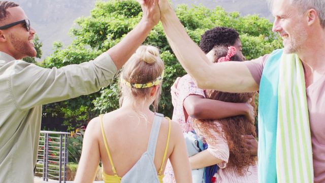 Diverse group of friends embracing and high-fiving outdoors, reflecting celebration and inclusivity. Ideal for concepts related to friendship, unity, celebration, lifestyle, and positive social interactions.