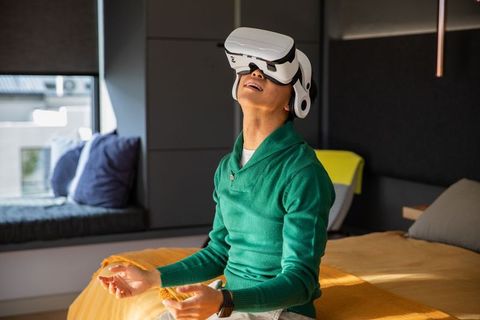 Asian man experiencing immersive virtual reality headset while relaxing on sunlit bed