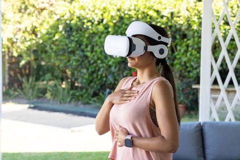 Woman practicing guided breathing with vr headset and smartwatch on outdoor patio