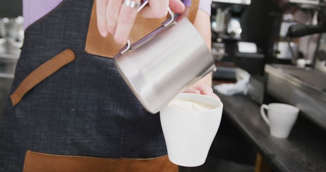 Caucasian male barista wearing apron adding milk to coffee in cafe. Local business owner and hospitality concept.