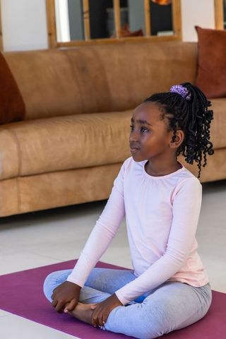African american girl practicing yoga at home seated cross-legged on purple mat calm focused