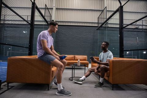 Two athletes relaxing and chatting in indoor court lounge between matches