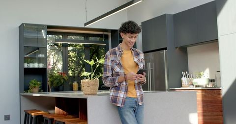 Casual Young Teen Engaging with Smartphone in Chic Modern Kitchen